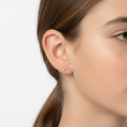 Close-up of an ear wearing gold stud earrings with a neutral background